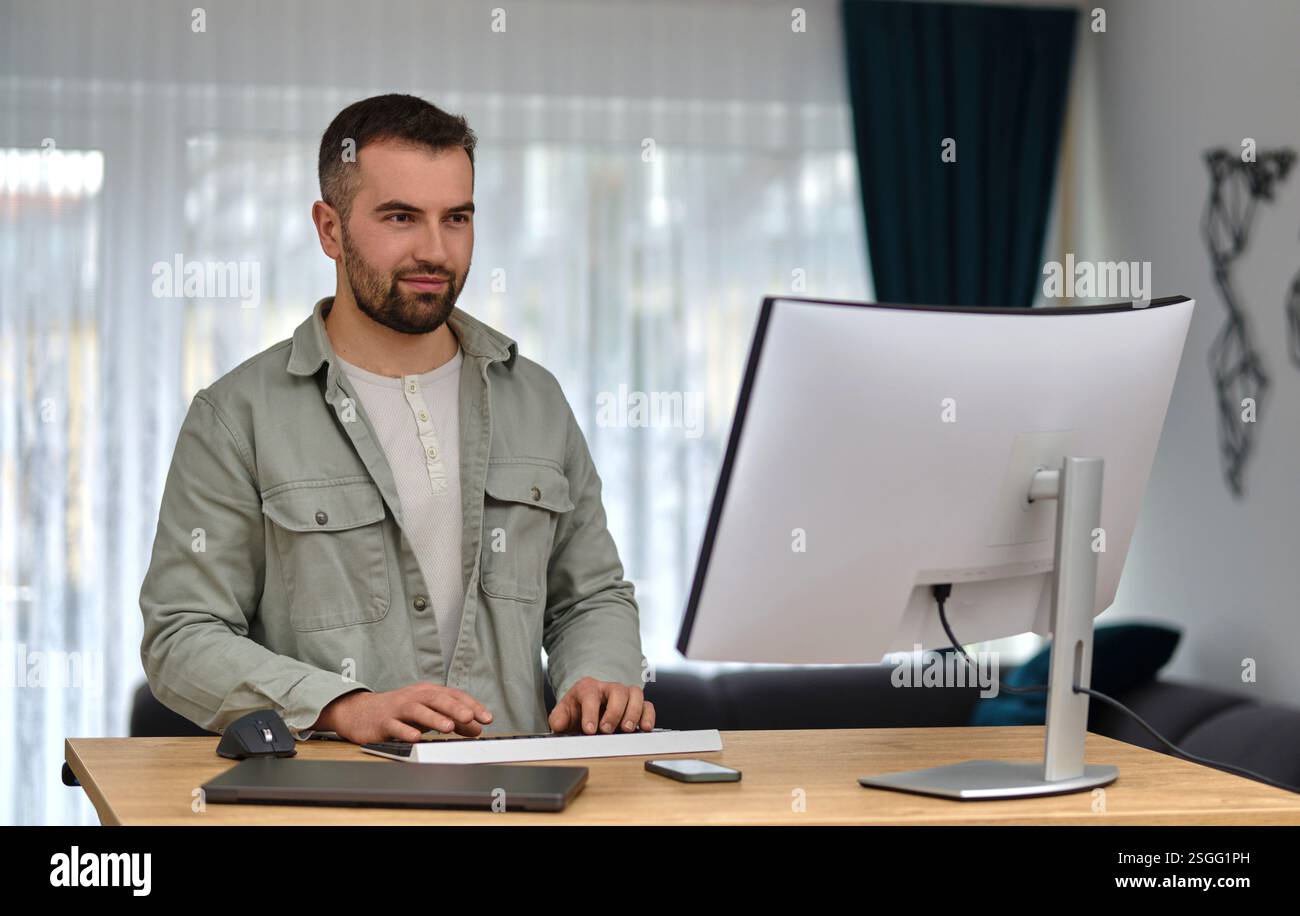 A happy man using a desktop computer while working at a home. Stock Photo