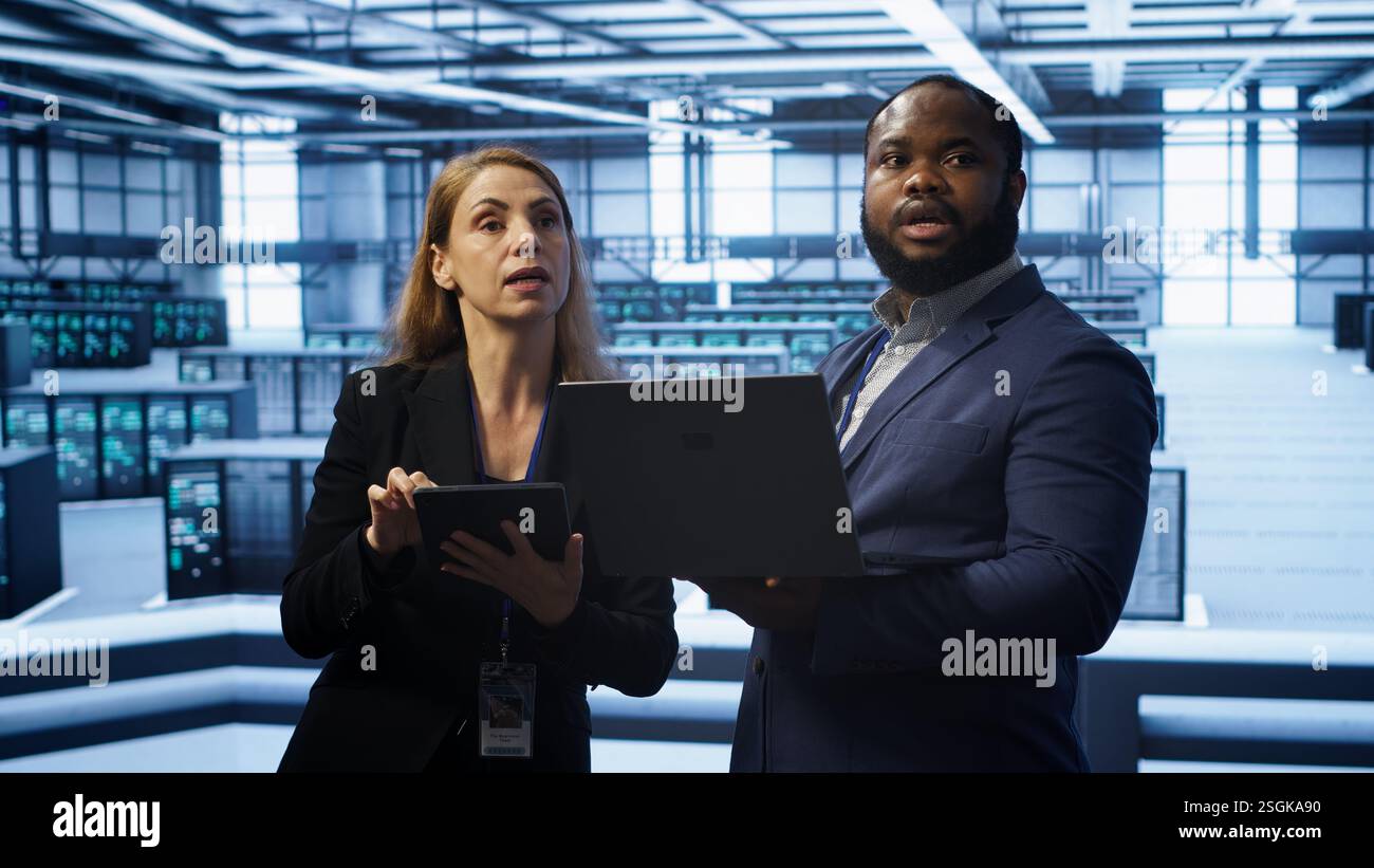 Manager in data center supervising worker running error checking utilities to fix errors. Supervisor in server farm overseeing engineer repairing network issues affecting rigs performance, camera A Stock Photo