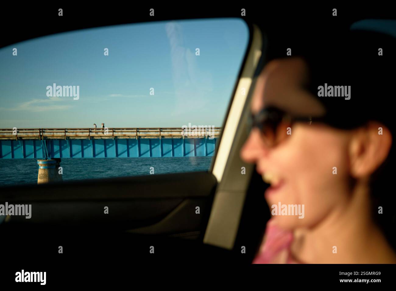Smiling Car Bridge Woman smiling inside car with blue bridge and two figures visible ...