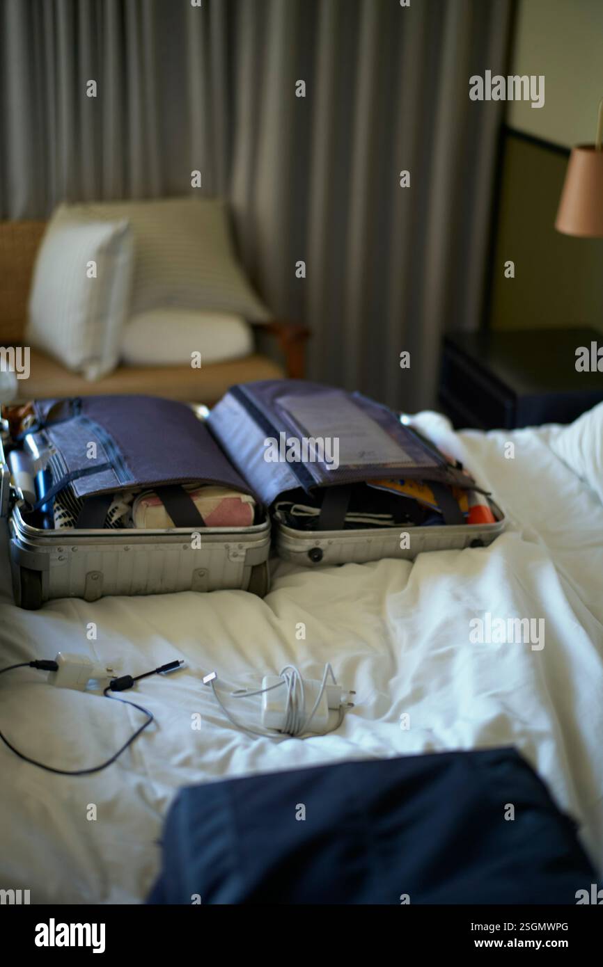 Open suitcase on a bed with clothes inside, hotel room setting with curtains and pillows, Miami, Florida, USA Stock Photo