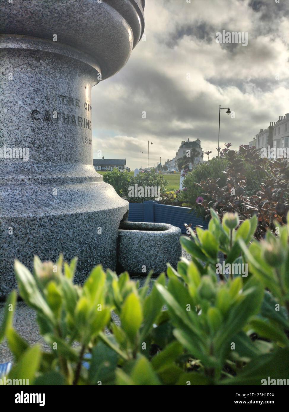 At a coastal path, a historic monument stands prominently amidst vibrant greenery. The sky is filled with dramatic clouds, creating a picturesque back - Smartphone Captured Stock Image