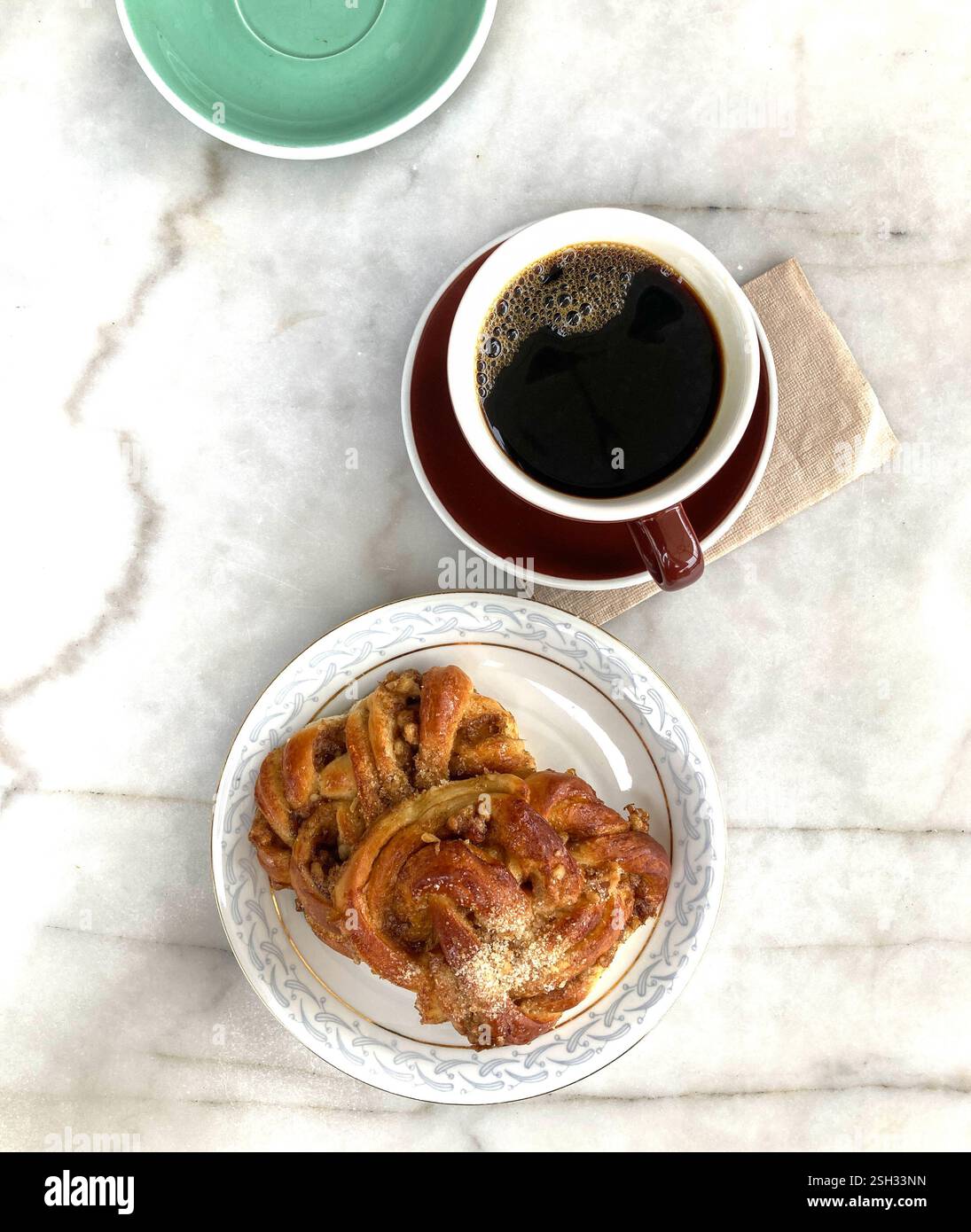 Photograph of a plate with pastries on, with cups and saucer, one filled with black coffee behind, all sitting on a marble table. - Smartphone Captured Stock Image