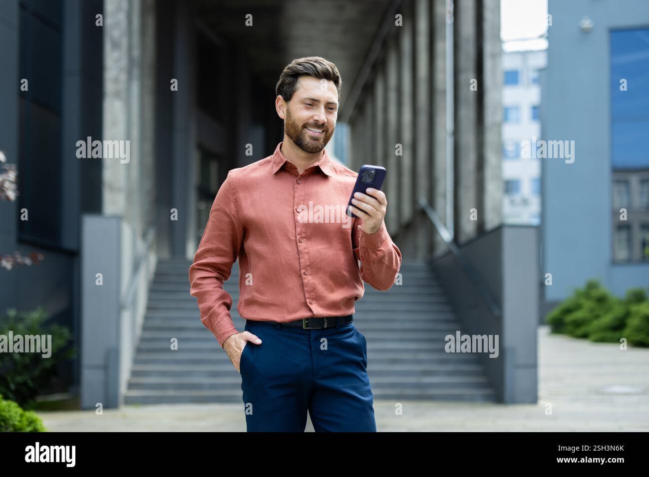 Confident Businessman Using Smartphone While Standing Outside an Office Building. Stock Photo