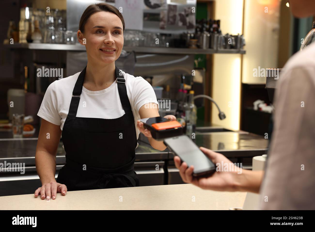 Cafe worker taking payment from client via terminal indoors Stock Photo ...