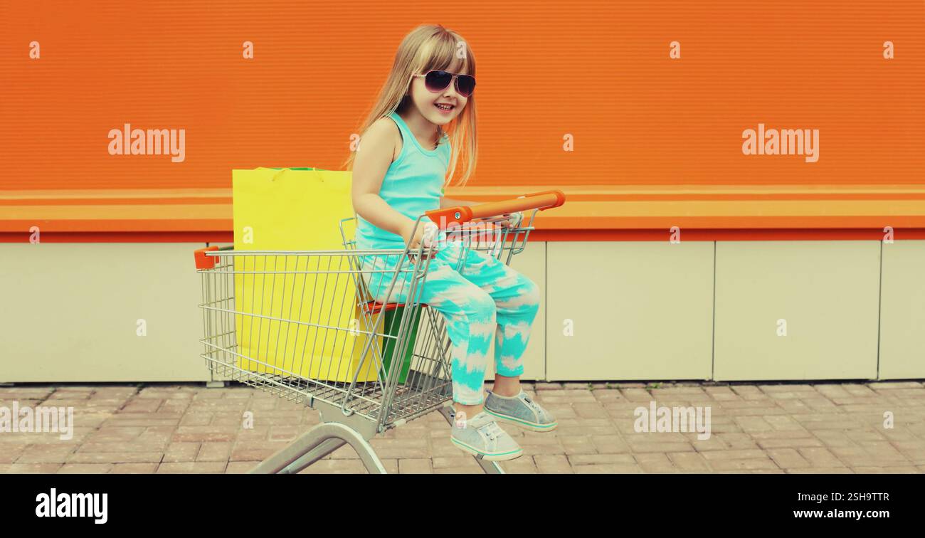 Happy little girl child sitting in trolley cart and colorful shopping ...