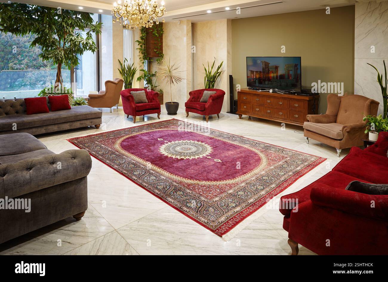 Luxurious living room with a vibrant red Persian rug, classic furniture, and marble floors. Stock Photo