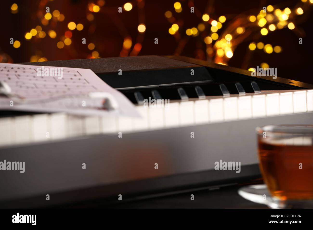 Piano with musical notes, earphones and cup of tea on table against blurred lights, closeup. Bokeh effect Stock Photo