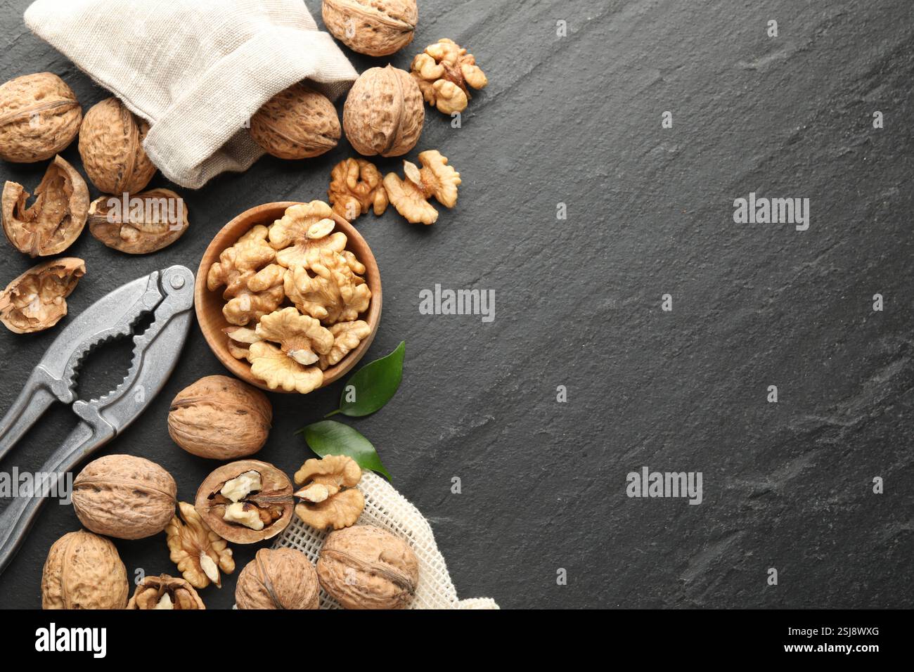 Fresh ripe walnuts, shells and nutcracker on black table, flat lay. Space for text Stock Photo