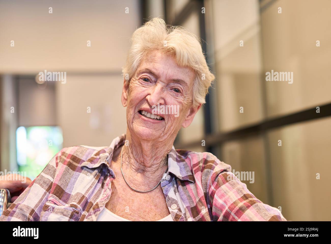 A cheerful elderly woman with white hair smiles warmly in a cozy and ...