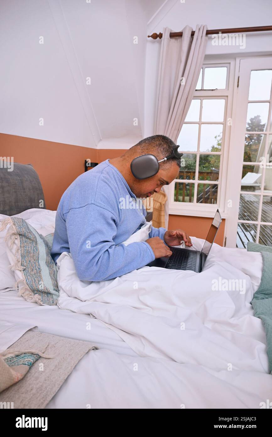 Man with Down Syndrome using laptop in bed Stock Photo