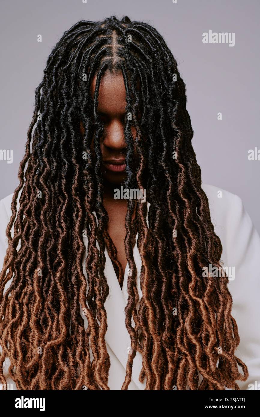 Young Black woman with long, curly locks smiling while looking down, showcasing beautiful natural hair with intricate patterns and textures Stock Photo