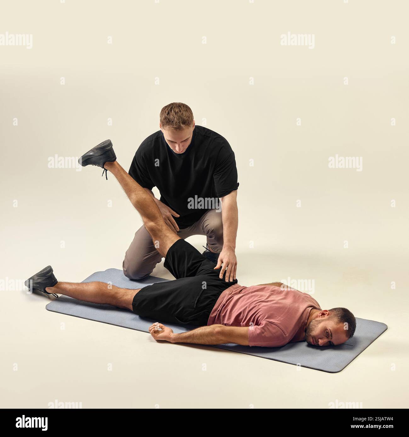 Trainer assisting man with prone leg raise, ensuring proper execution ...