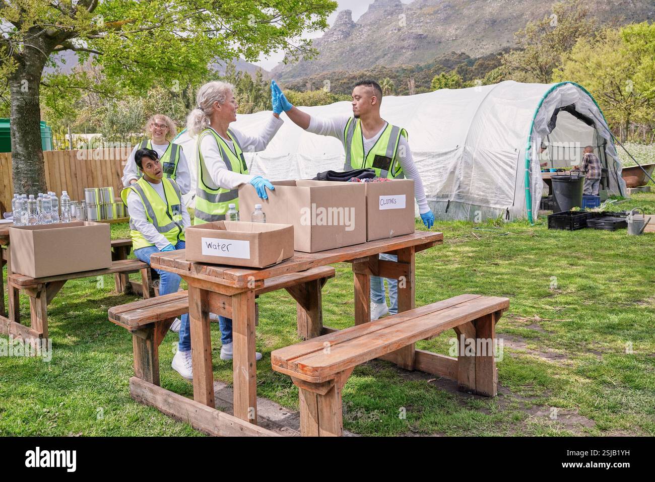 Two volunteers doing high five over donation boxes at table outdoors Stock Photo
