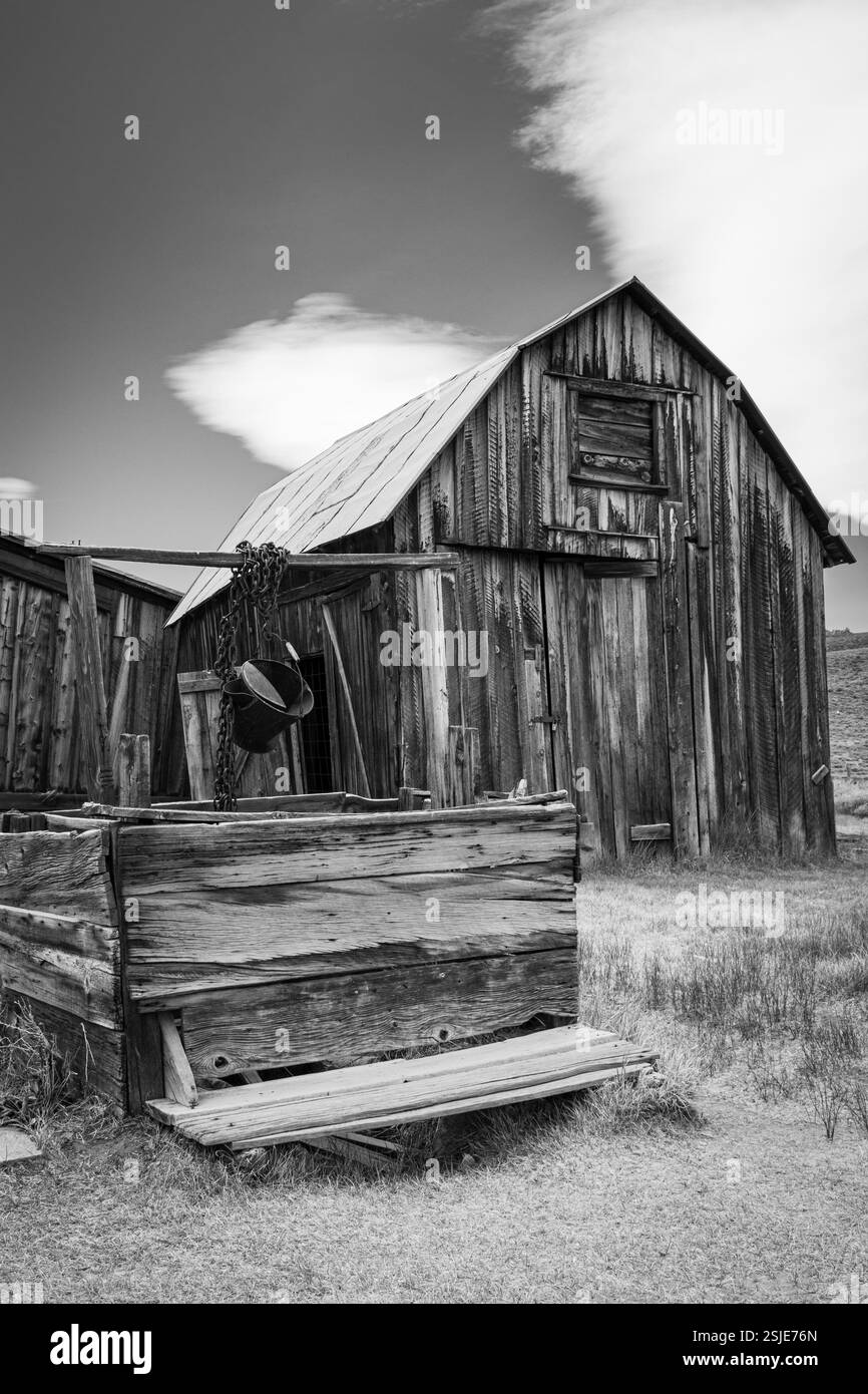 An old wooden barn with a well and bucket to draw water in Bodie ghost town. Black and white rural picture. Stock Photo