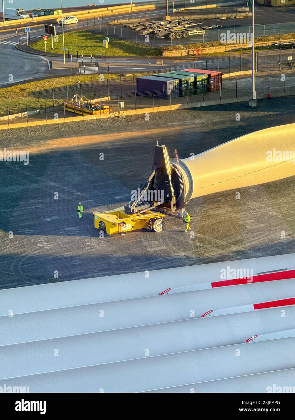 Le Havre, France, Europe - 16 January 2025: Workers using specialist remote controlled transporting equipment to move a large wind turbine blade - Smartphone Captured Stock Image