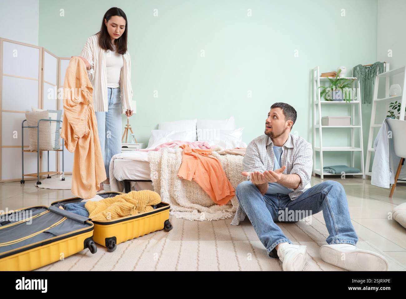 Upset young woman packing clothes and her husband in bedroom. Cheating ...
