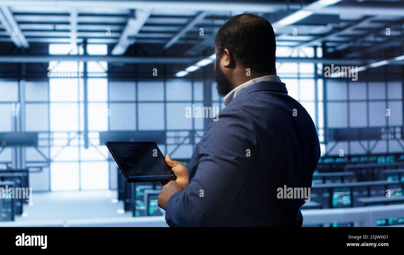 IT operator in server room workspace using tablet to patch network issues affecting transfer rates. Engineer in data center fixing errors affecting server rows rigs, camera A Stock Photo