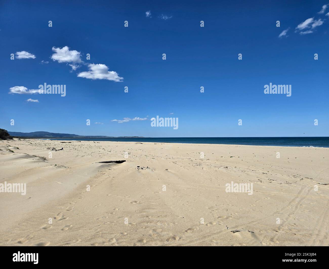 fluffy white clouds floating across a clear blue sky above a large sandy beach - Smartphone Captured Stock Image