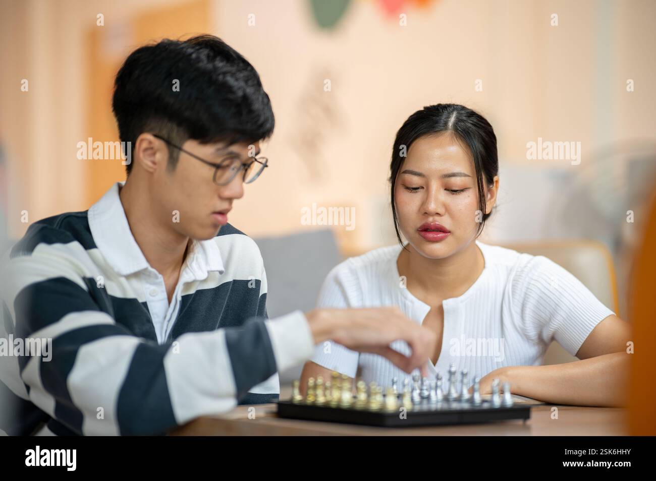 A beautiful Asian woman plays chess seriously with her friend in the living room. leisure, activity, entertainment Stock Photo