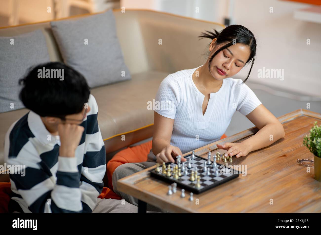 A beautiful, serious Asian woman plays chess seriously with her friend in the living room. leisure, activity, entertainment Stock Photo