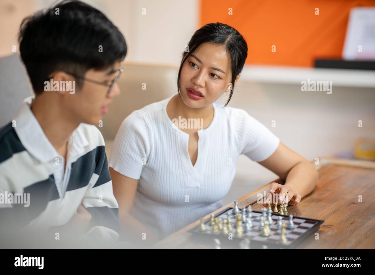 A beautiful, serious Asian woman plays chess seriously with her friend in the living room. leisure, activity, entertainment Stock Photo