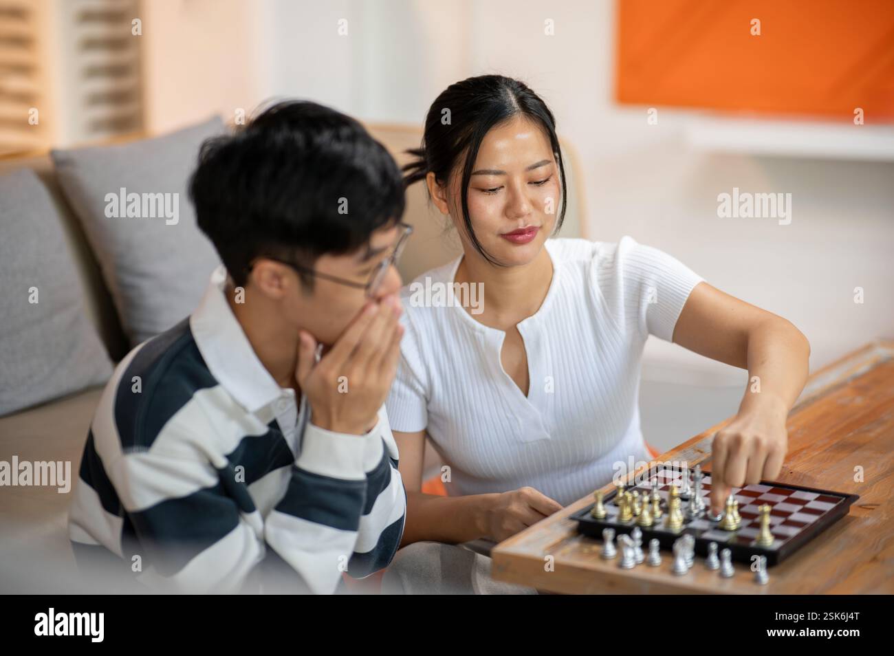 Two happy Asian male and female friends are enjoy playing chess together in the living room. leisure activity, entertainment, board game Stock Photo