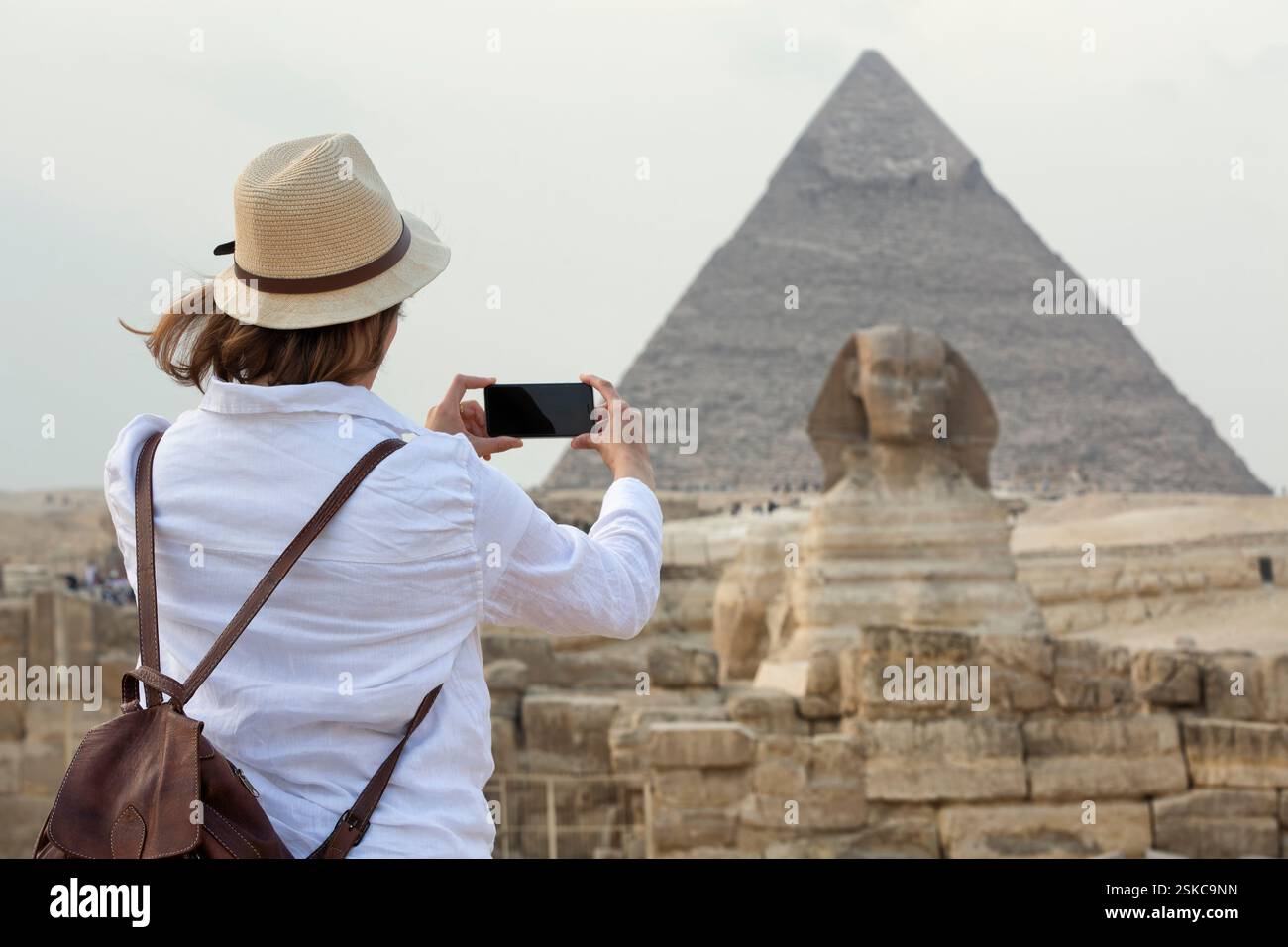 young woman standing taking a photo in front of the Great Sphinx of ...