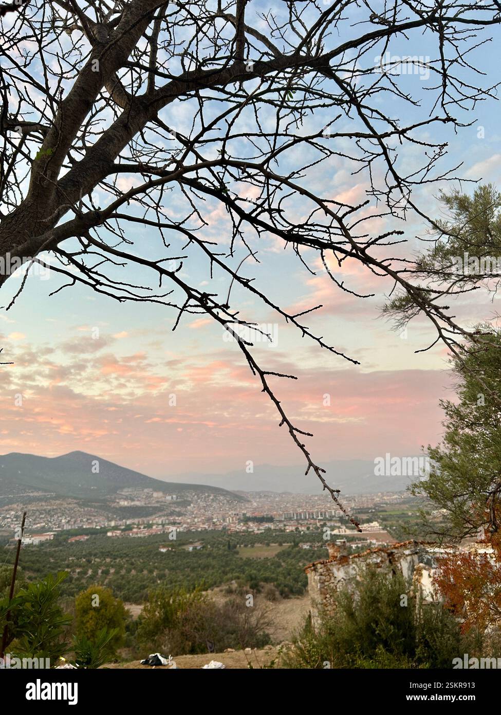 Beautiful view of a city at sunset, surrounded by mountains and trees - Smartphone Captured Stock Image