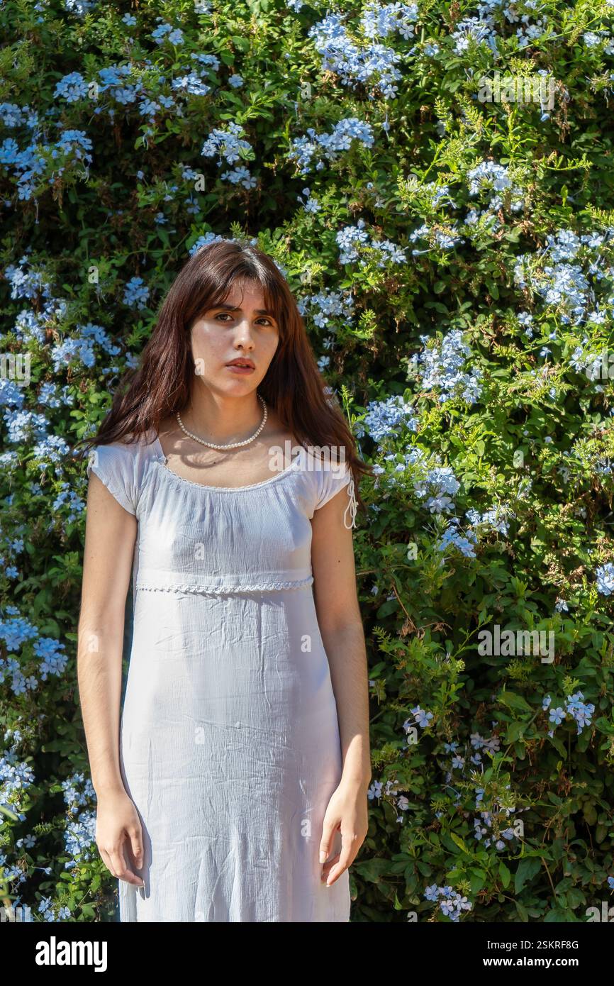 Fashion model posing in front of a flowering hedge wearing a white ...