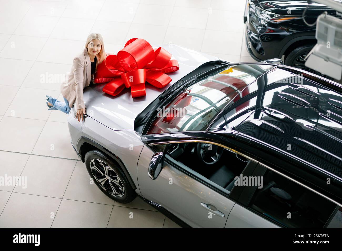 Happy customer admiring her brand new car with a big red bow on top ...
