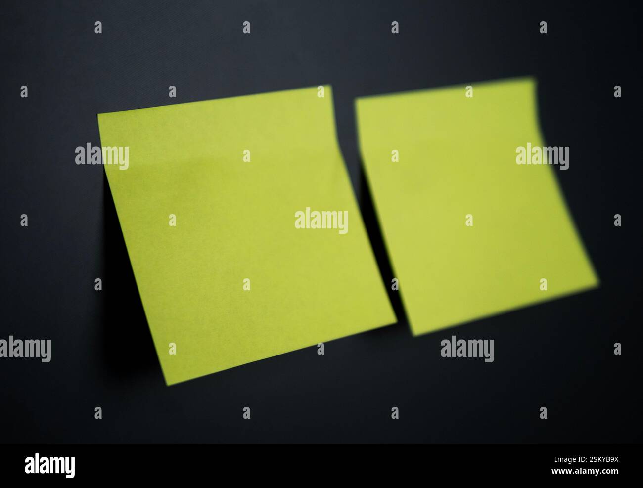 Two empty yellow sticky notes are placed on a black surface, ready for writing Stock Photo