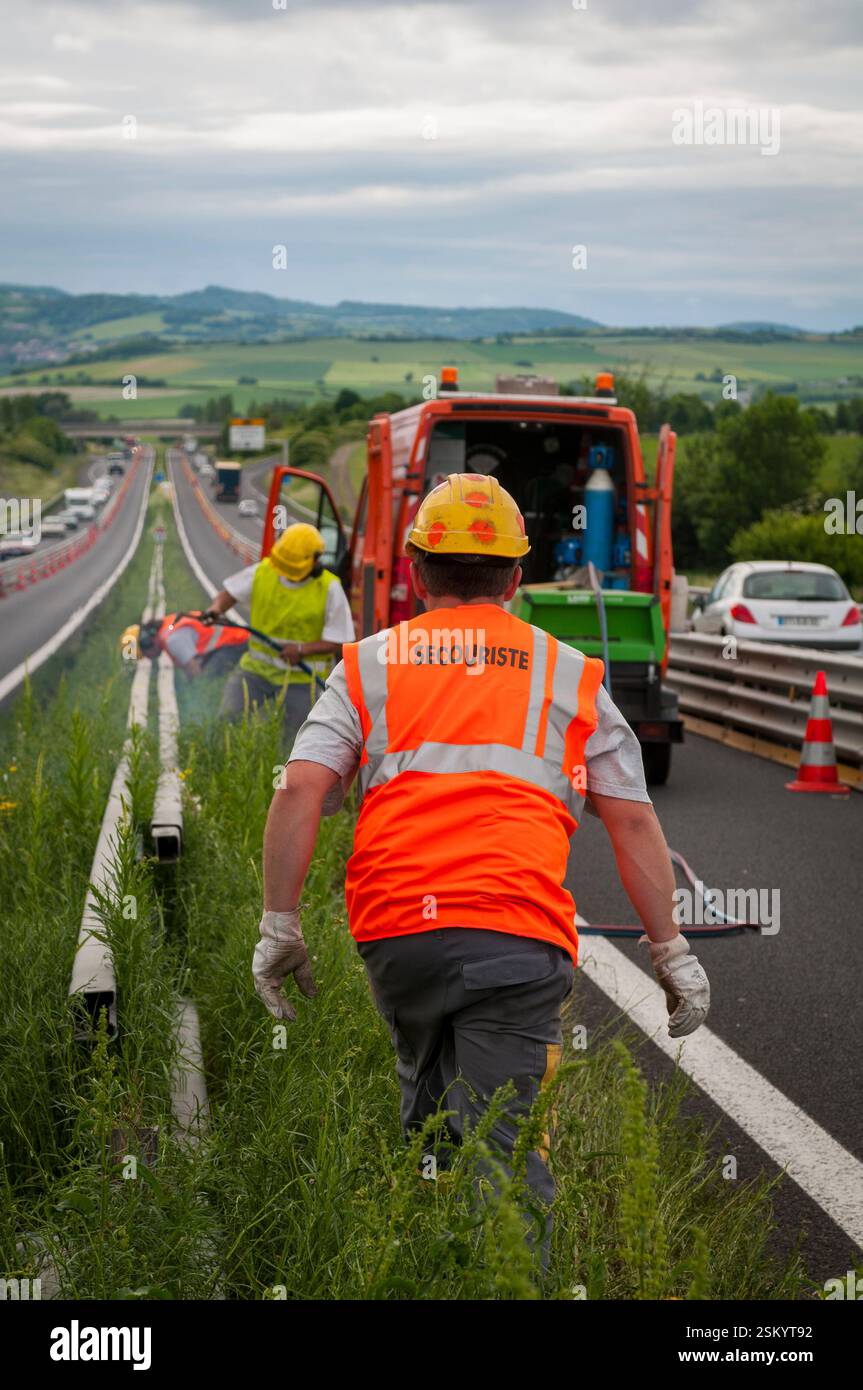 A75 motorway. Dismantling of the safety barriers on the central reservation, overgrown with weeds, in order to replace them with a concrete separator. Stock Photo