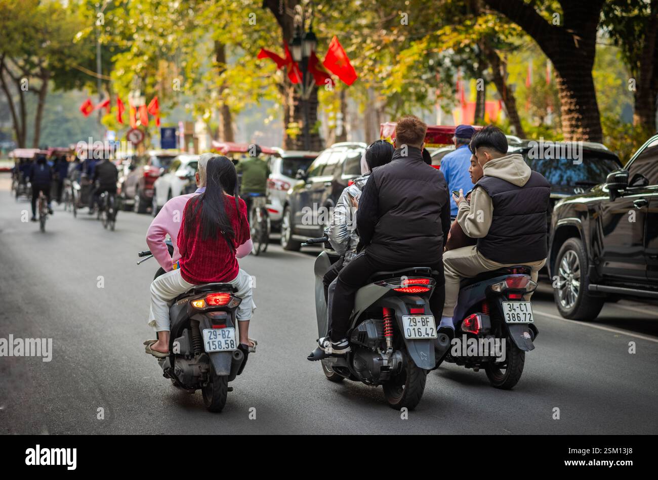 A group of young Vietnamese friends on three motorcycle scooters and not wearing helmets cruise down a road near Hoan Kien Lake in central Hanoi, Viet Stock Photo