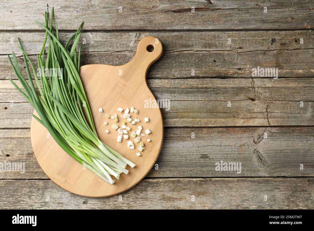 Cutting board and green onions on wooden table, top view. Space for ...