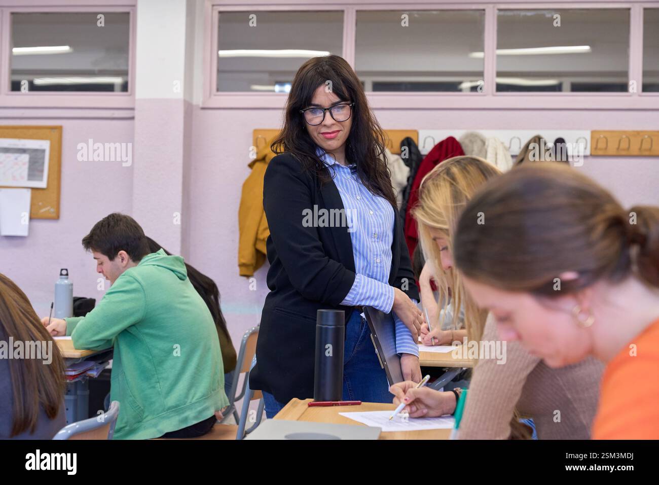 University professor supervising students taking exam in classroom ...