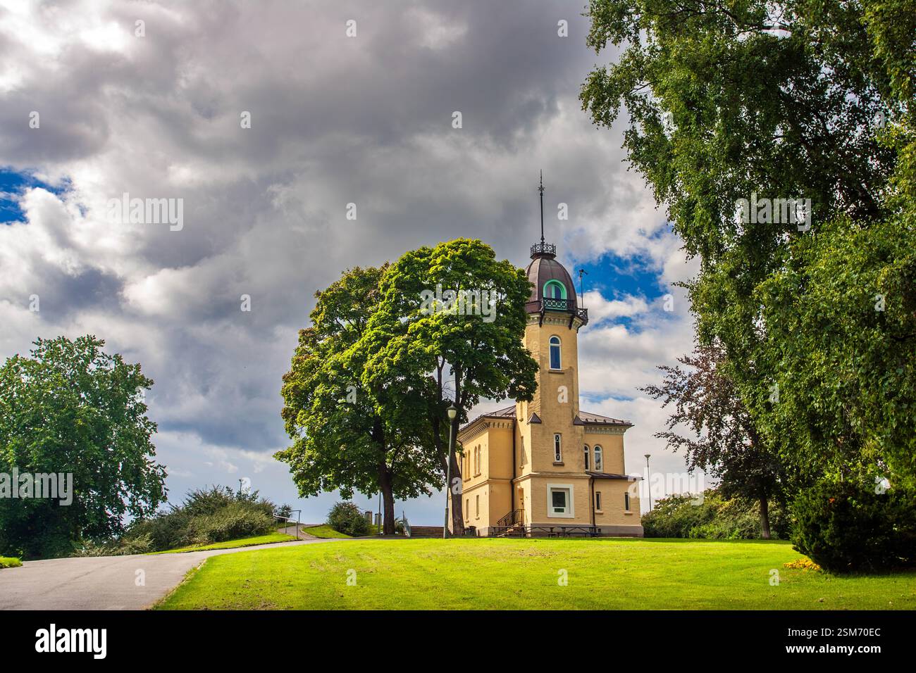 Tall tower house stands surrounded by green trees under a cloudy sky at St. Hanshaugen park in Oslo, Norway, inviting visitors to explore. Stock Photo