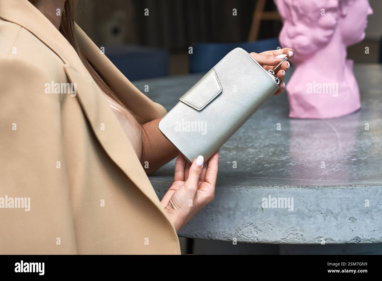 Sophisticated woman presenting stylish, beige, leather wallet at dining, elegant, setting, accessory, fashion, concept Stock Photo