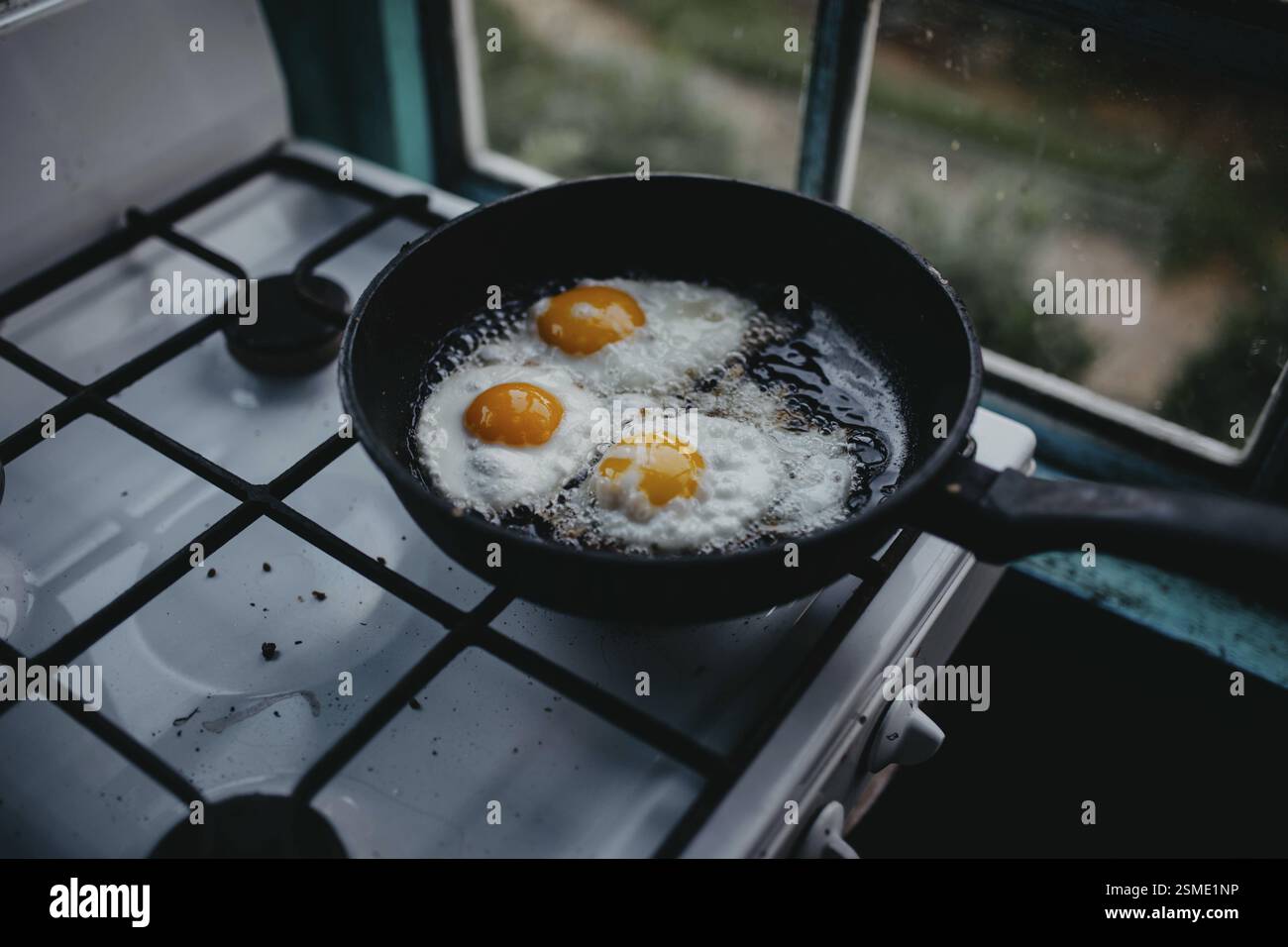 Frying pan with three eggs cooking on a gas stove beside a window Stock ...