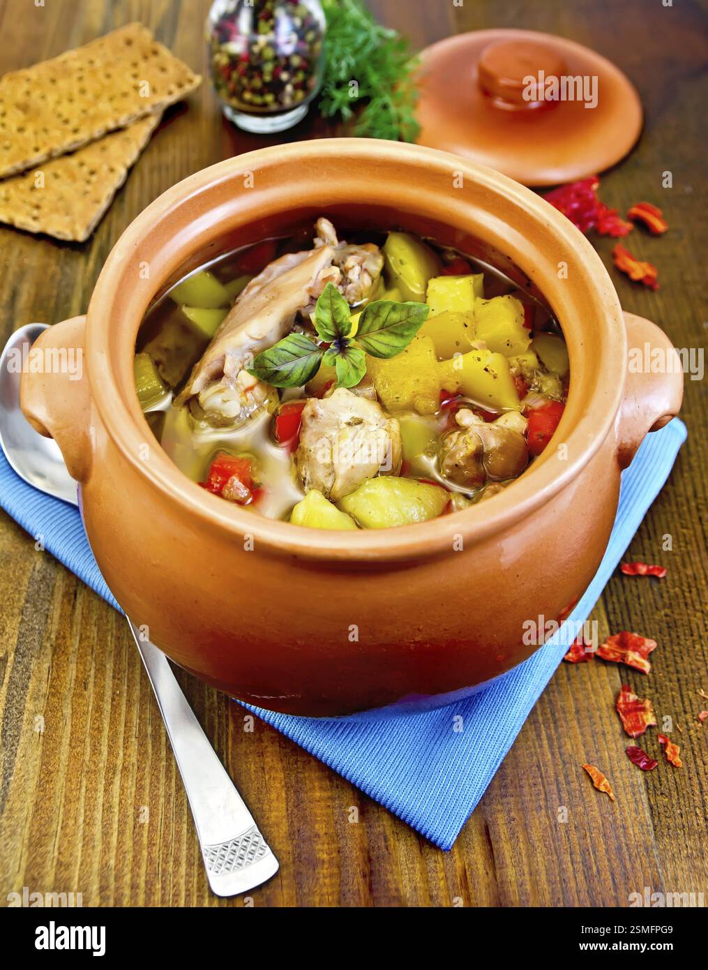 Roast with chicken meat, potatoes in a clay pot, napkin, spoon, crispbreads, dill, pepper in a jar, red hot pepper on board Stock Photo