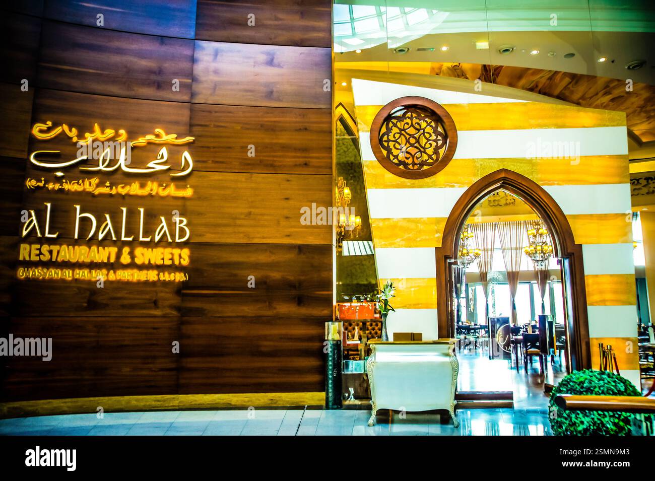 A Dubai restaurant entrance with Arabic writing translating to 'Al Hallab Restaurant & Sweets,' likely located in a shopping mall. 'Al Hallab' means ' Stock Photo