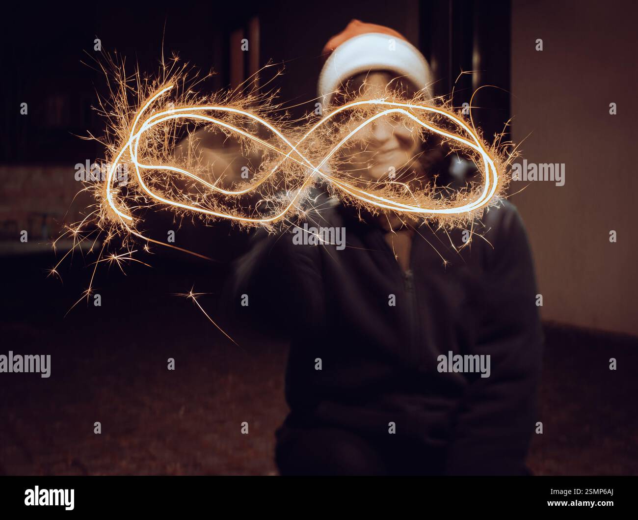 Girl painting with freeze light. Festive freezing lights in the night. Sparkling forms made by woman in Santa hat. Stop light drawings. New Year fun Stock Photo
