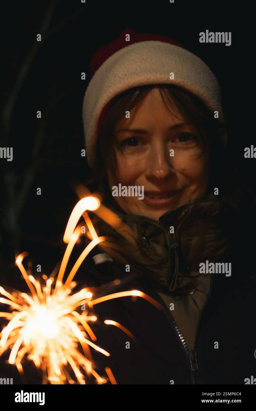 Girl painting with freeze light. Festive freezing lights in the night. Sparkling forms made by woman in Santa hat. Stop light drawings. New Year fun Stock Photo