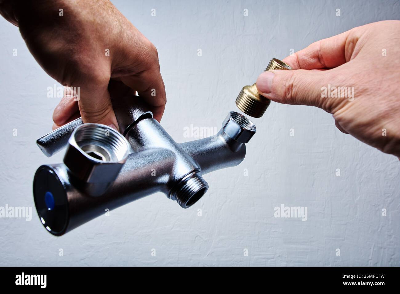 Plumbing fixture of bathroom mixer tap with brass brass eccentric reducer being connected by person hands. Stock Photo