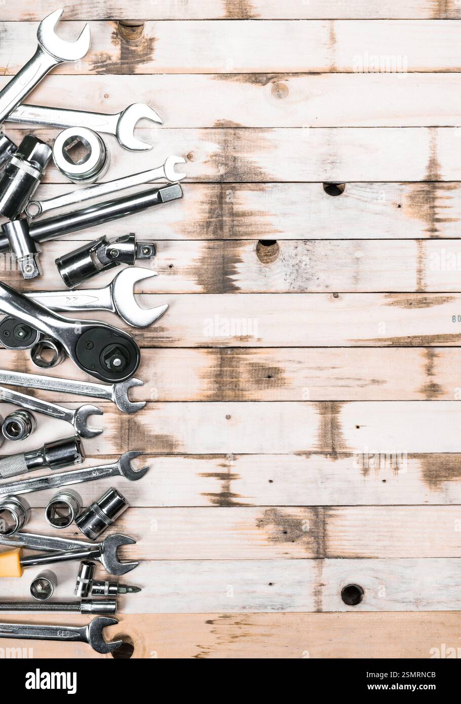 Assorted tools including wrenches and sockets arranged on a rustic wooden surface in a workshop setting Stock Photo
