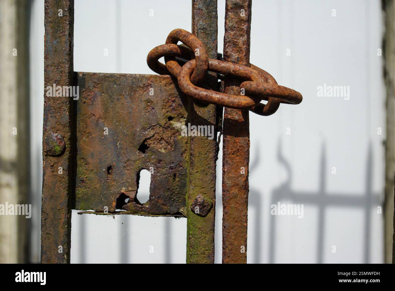Heavy rusty chain securing a church gate, shadows of the gate on a white wall behind, UK Stock Photo