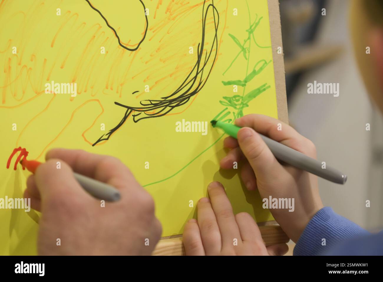 Two children share a creative moment, using green and red markers to draw on a large sheet of yellow paper at a community center art session. Stock Photo