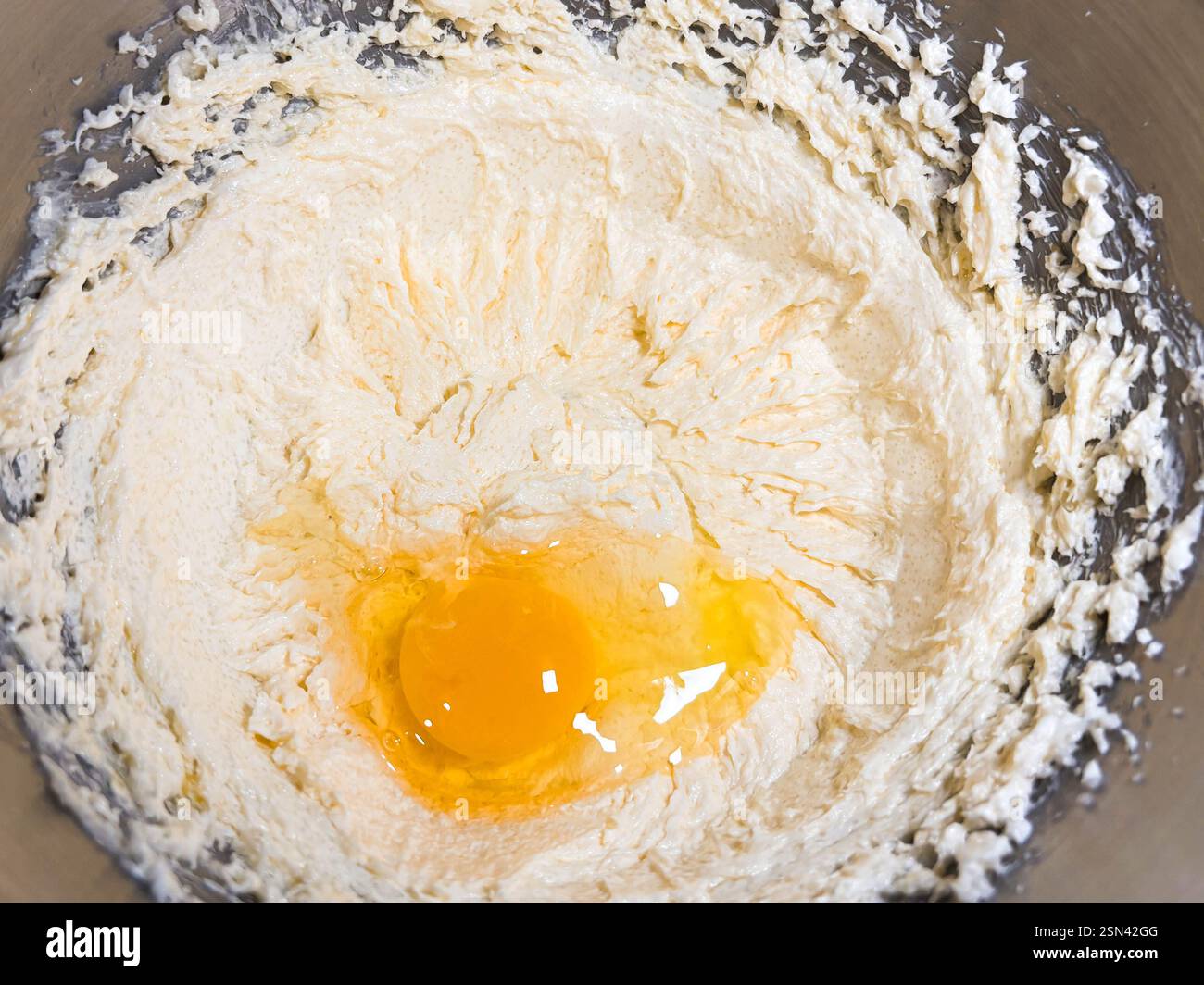 Beating butter, sugar and eggs in a grey metal bowl. The process of making cake and cookies by mixing butter, eggs and sugar. Close-up of an egg in cr Stock Photo