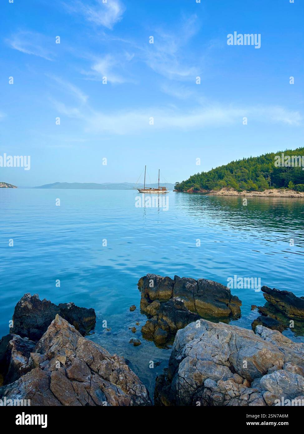 Beautiful clear blue waters of the Mediterranean Sea with views of a boat, mountains, and rocks - Smartphone Captured Stock Image