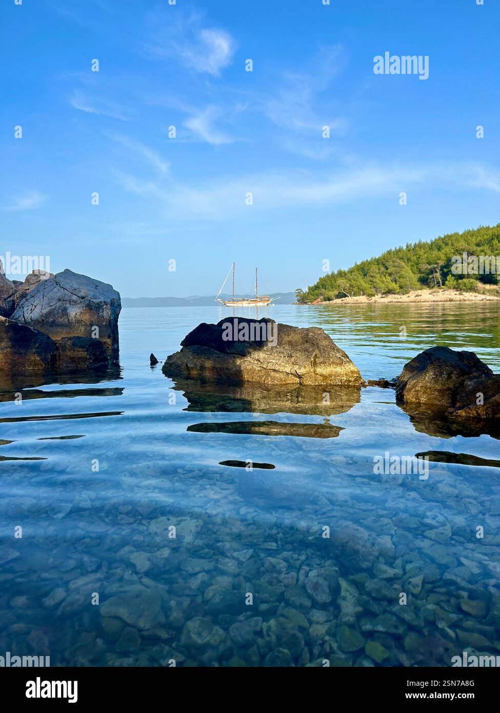 Beautiful clear blue waters of the Mediterranean Sea with views of a boat, mountains, and rocks - Smartphone Captured Stock Image