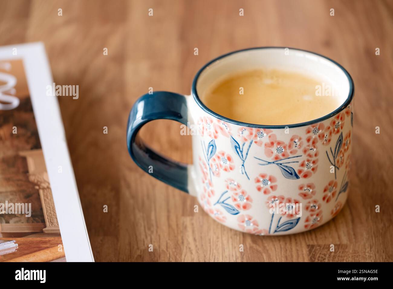 Bristol, UK. A cup of hot coffee served in a china mug. The drink is served in the mug on a plain table background next to a magazine Stock Photo